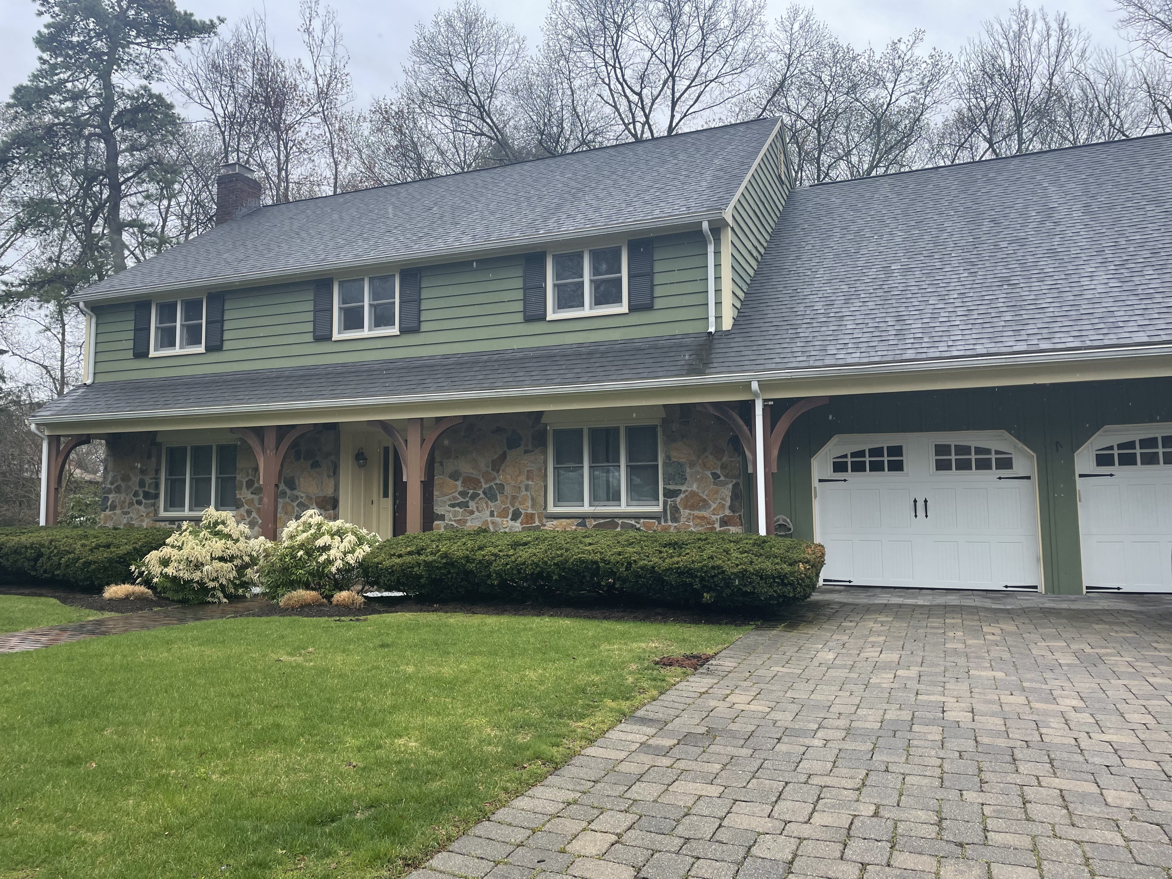 Green colonial home with stone facade in Lexington, MA after a new architectural shingle roof and seamless gutter installation by Storm King Roofing