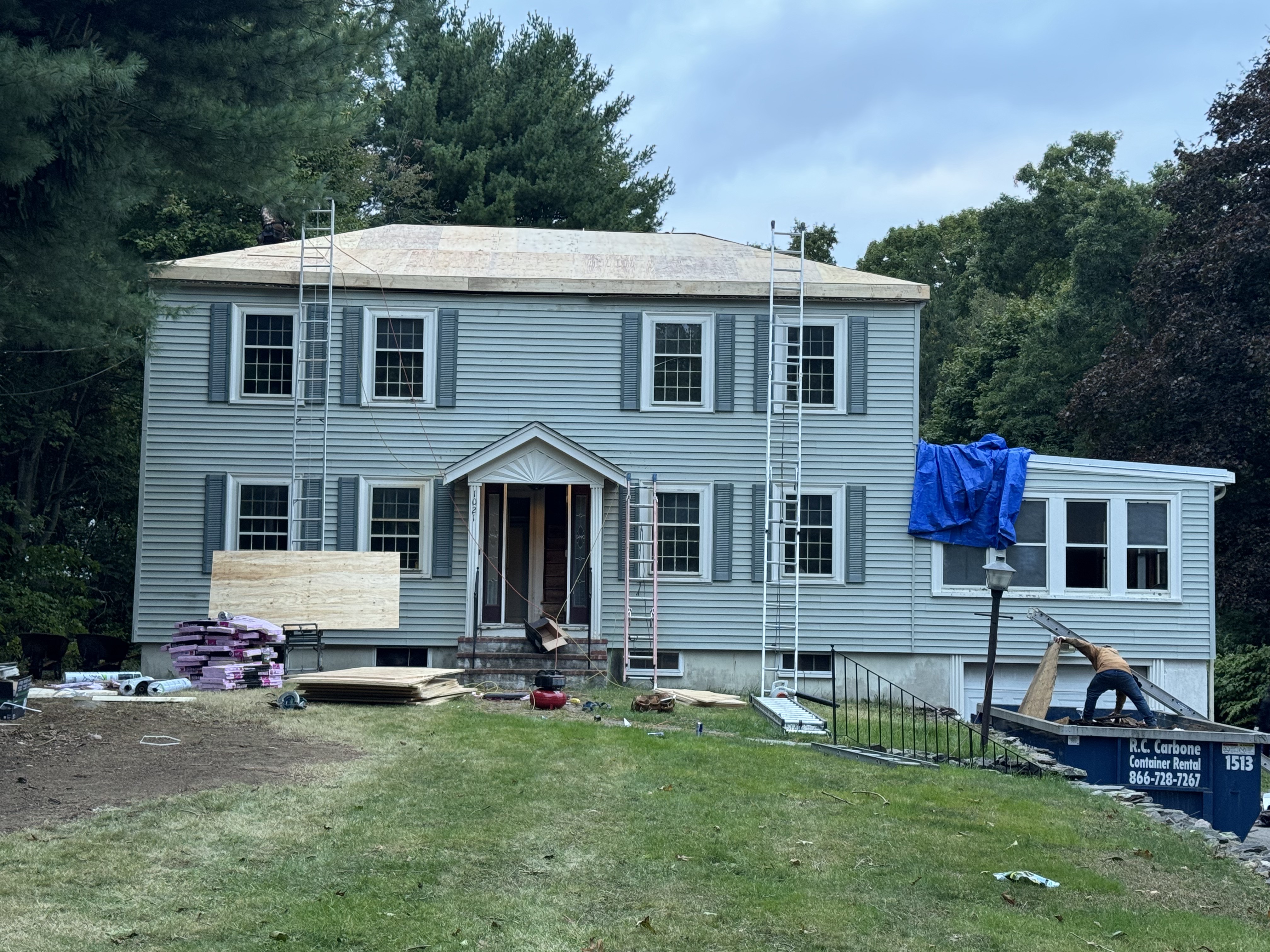 Gray colonial home in Brockton, MA mid-siding-installation with exposed sheathing and a Storm King Roofing dumpster on site