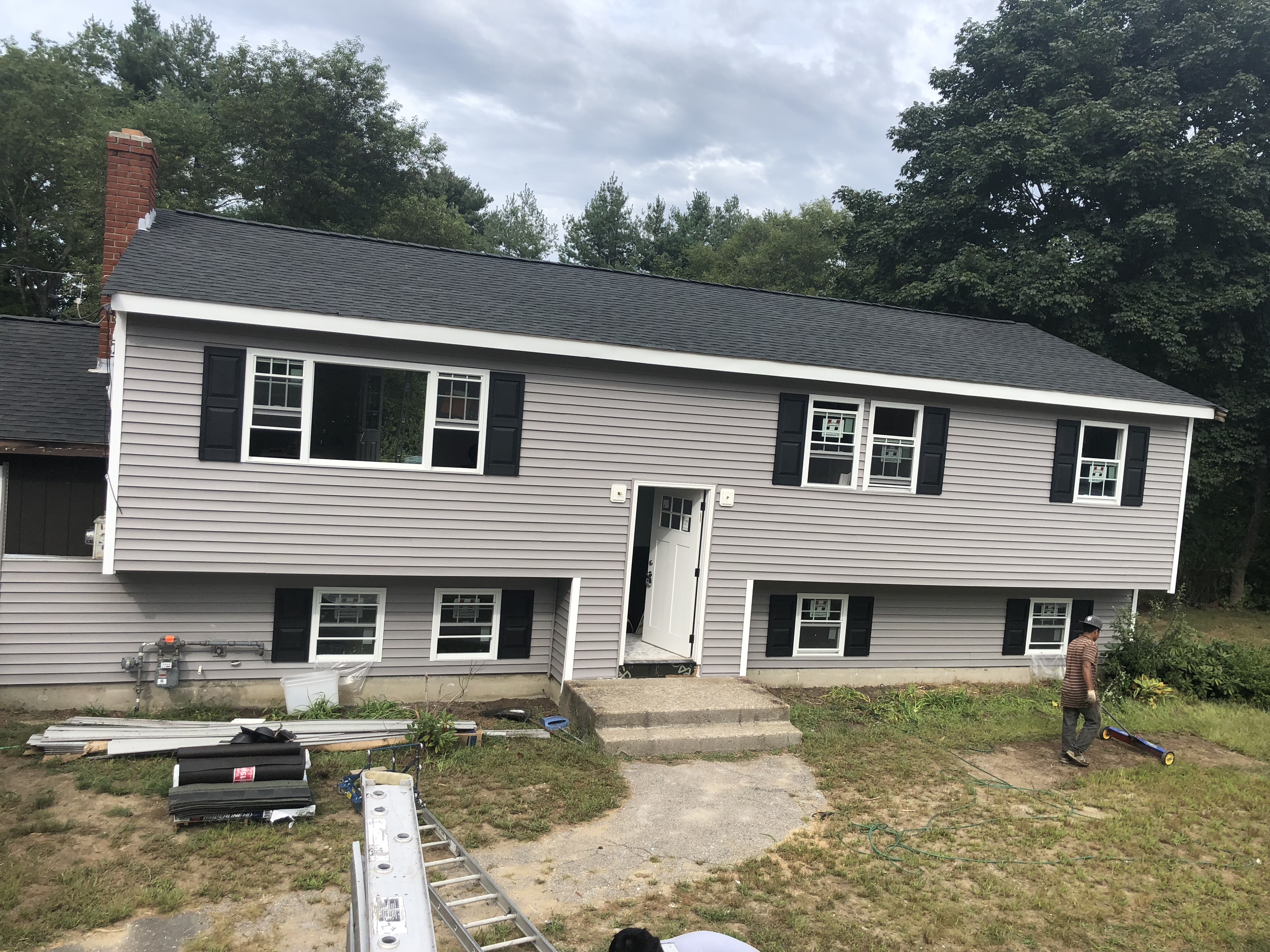 Completed dark architectural shingle roof and gray siding on a home in Hanson, MA with a Storm King crew member cleaning up